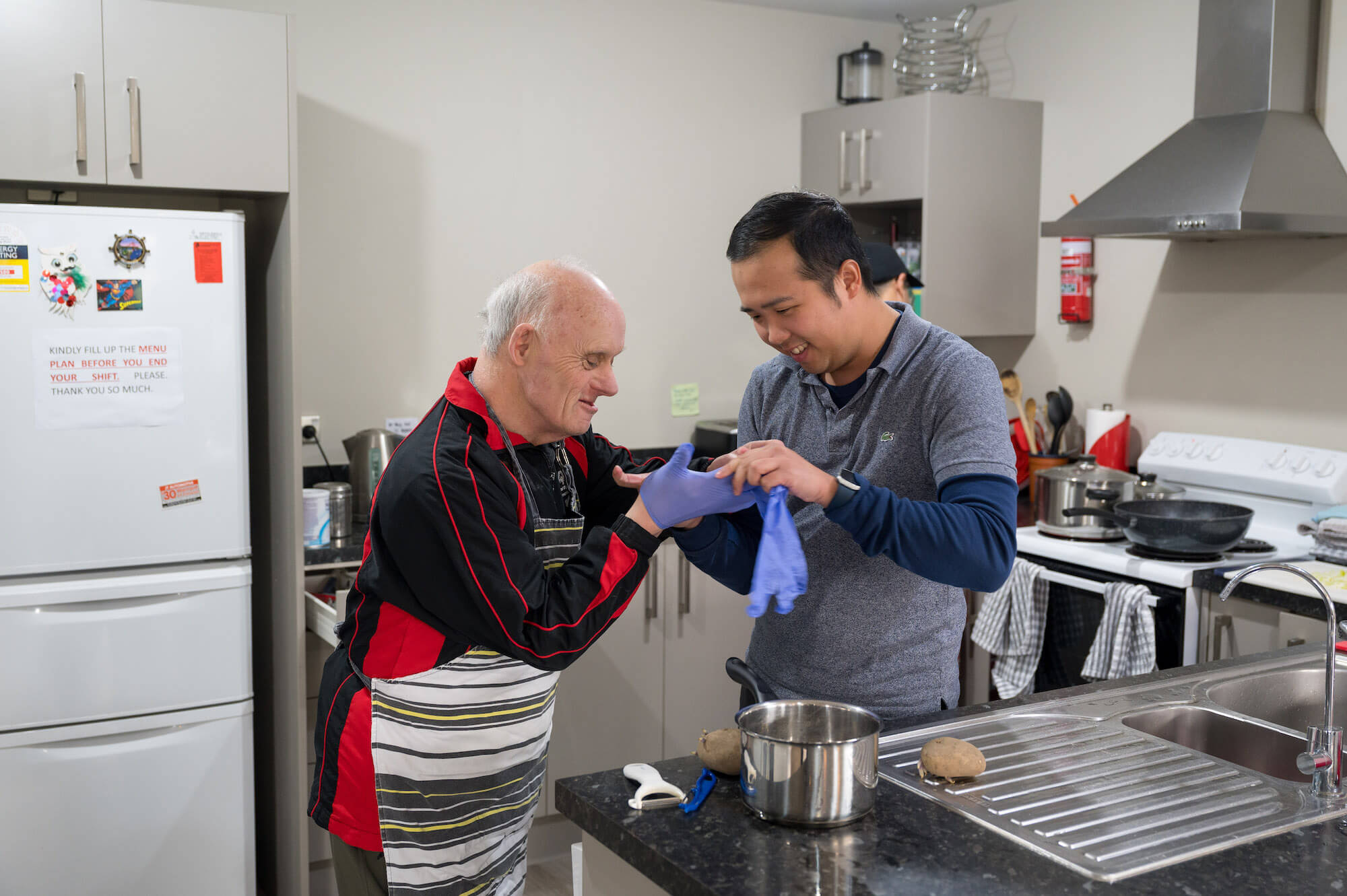 a person helping another person put on gloves in a kitchen