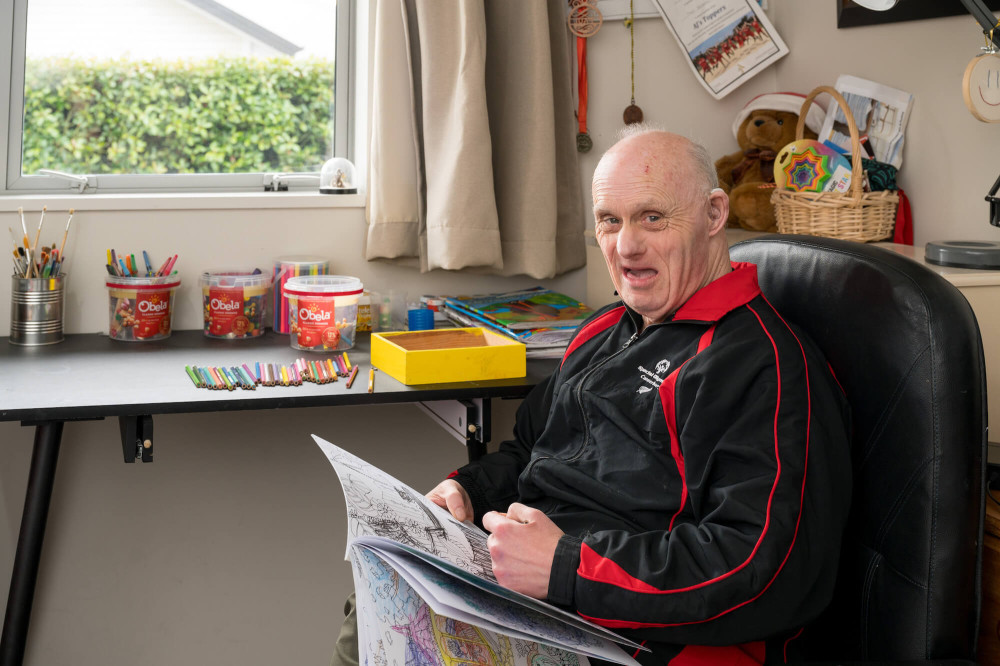 a person sitting holding a colouring book with art supplies on the desk behing them