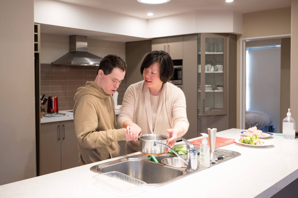 people in a kitchen holding a pot over a sink